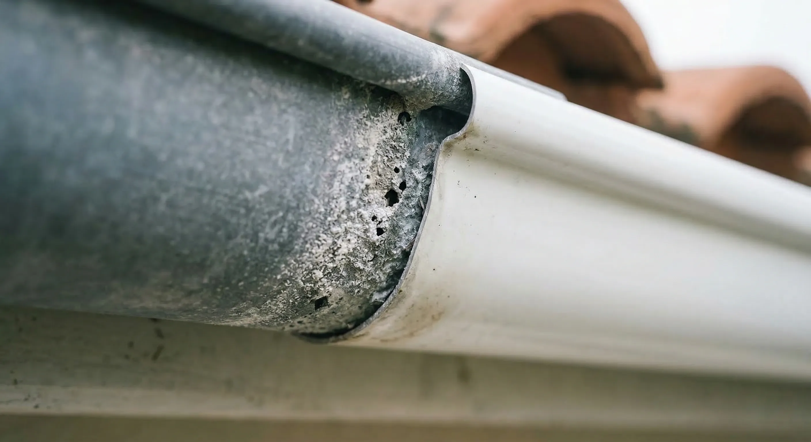 Gros plan sur une jonction zinc-aluminium corrodée par effet galvanique, poudre blanche et micro-perforations visibles au point de contact