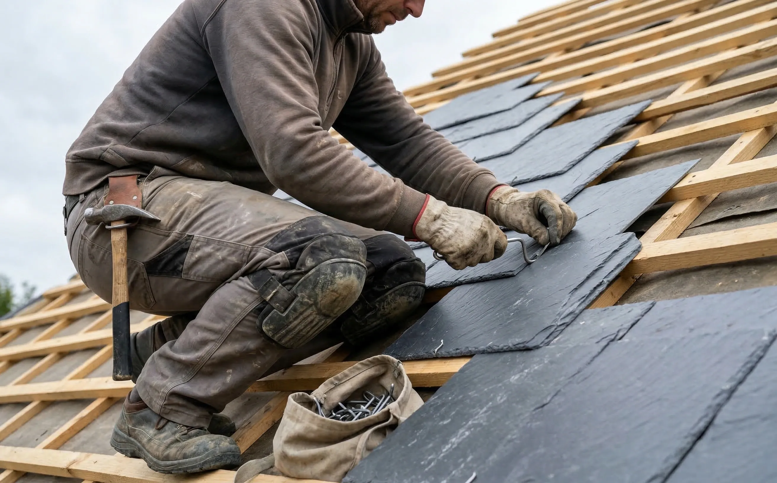 Couvreur posant des ardoises au crochet sur un liteaunage en bois, vue rapprochée des mains