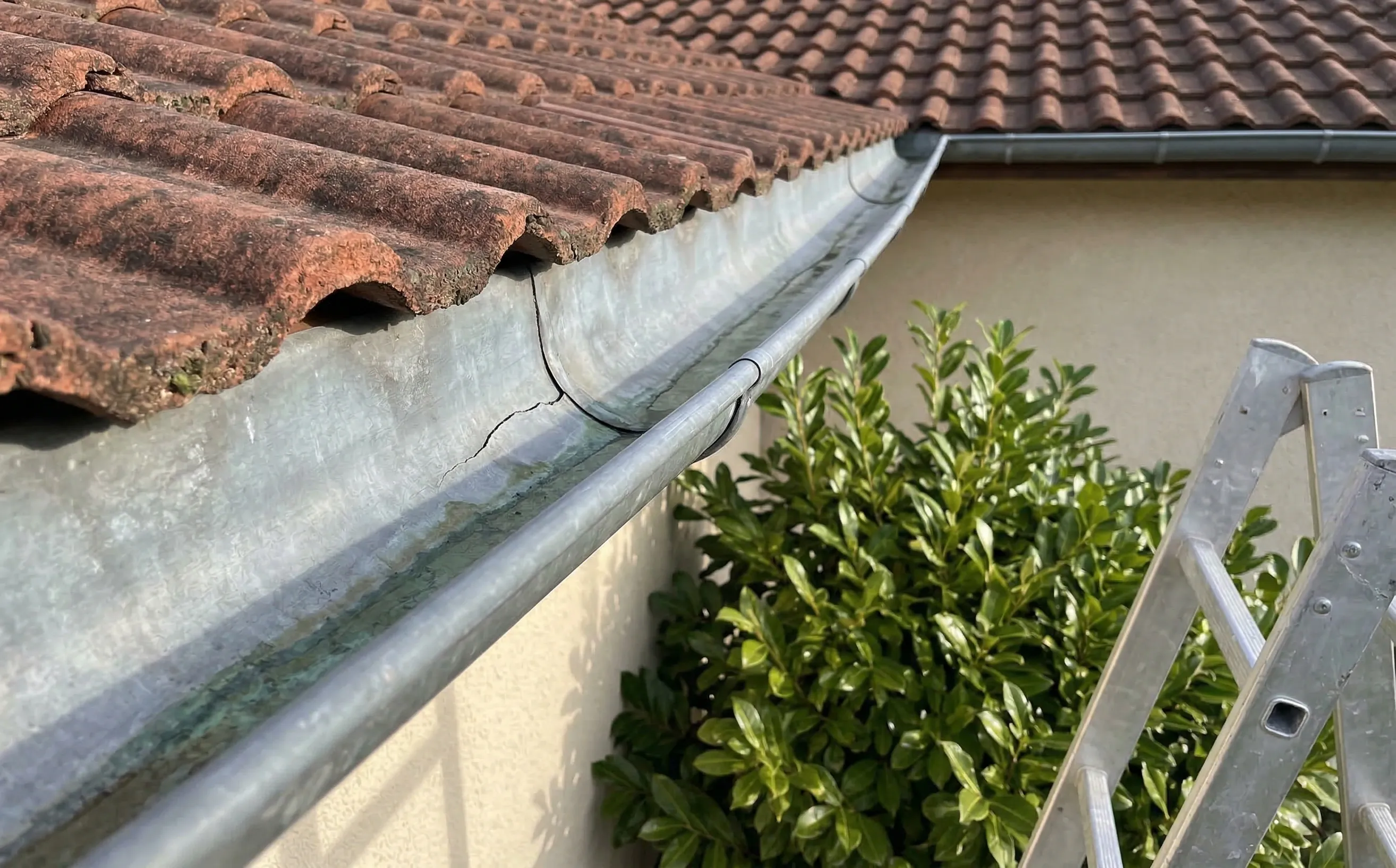Gouttière en zinc demi-ronde avec fissure visible le long d'un pli, fixée sous la rive d'un pavillon aux tuiles mécaniques