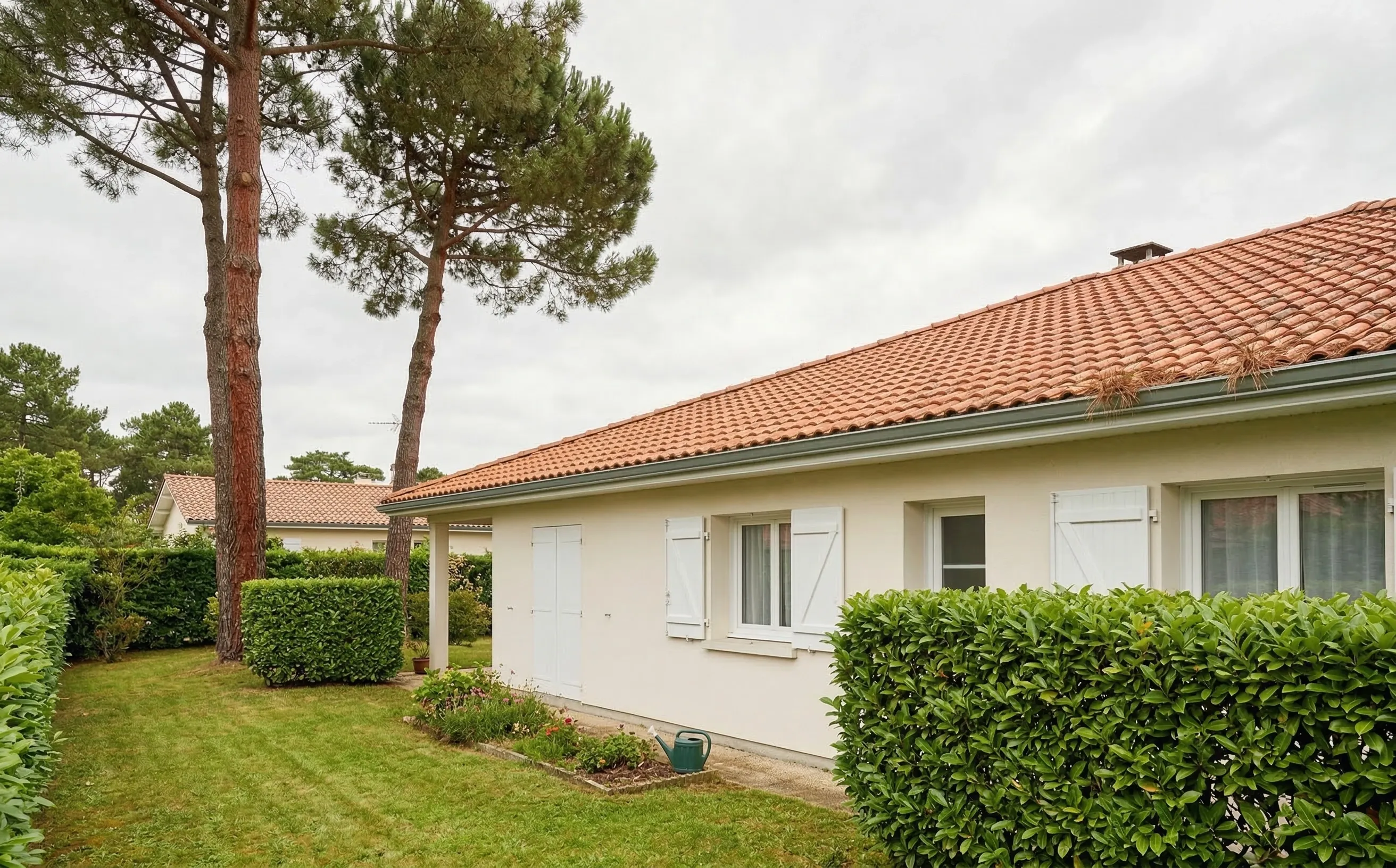 Pavillon résidentiel en Gironde avec toiture en tuiles mécaniques, pins maritimes en arrière-plan et ciel gris atlantique