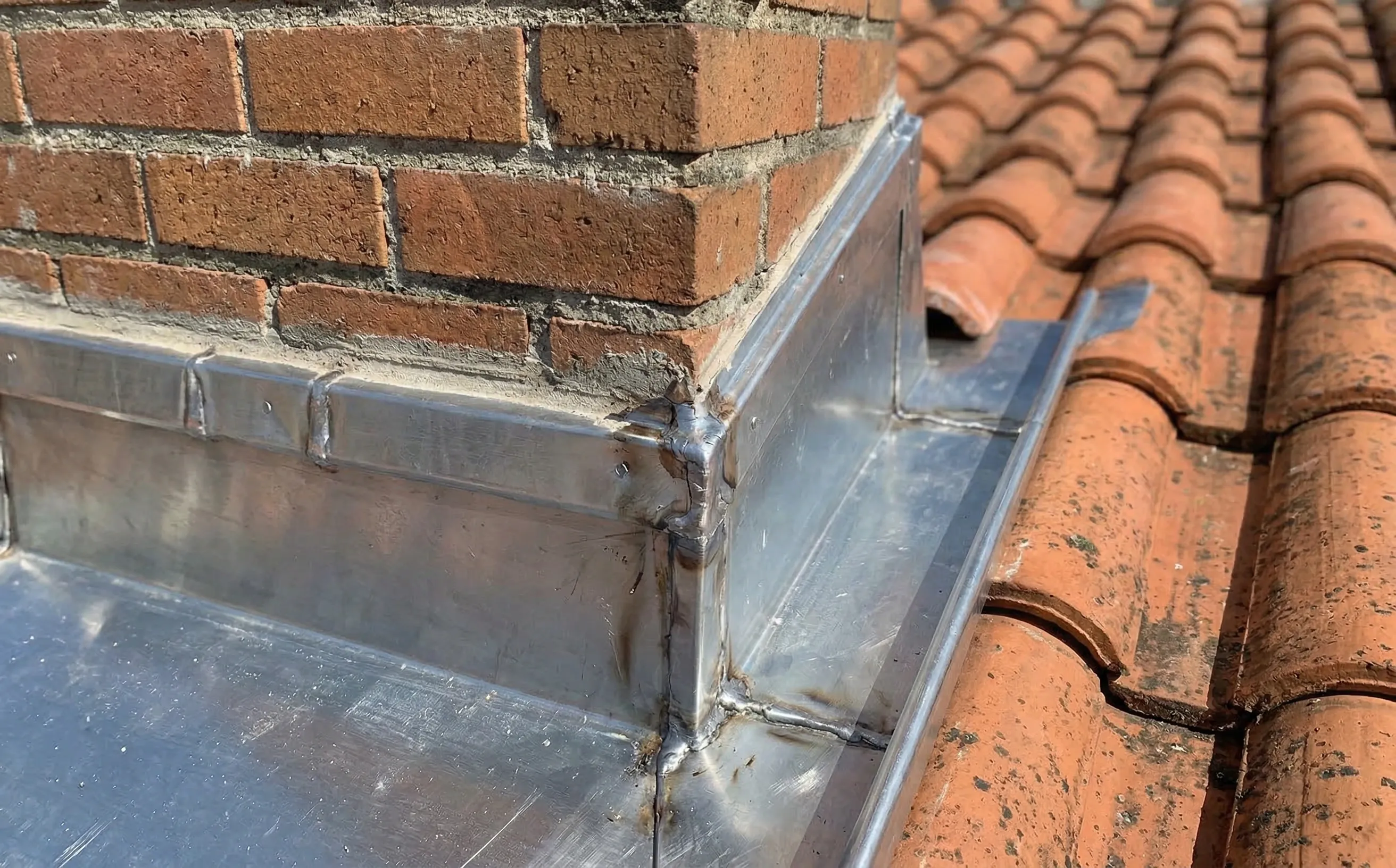 Vue rapprochée des quatre pièces d'un abergement en zinc assemblées autour d'une souche de cheminée