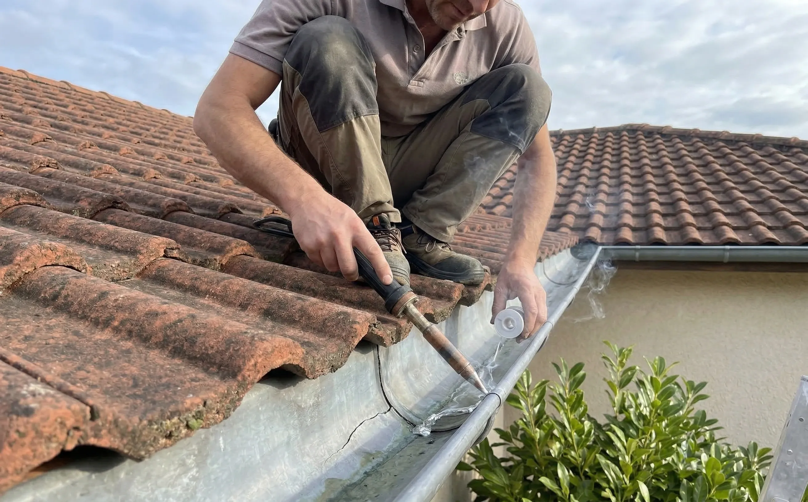 Couvreur-zingueur soudant à l'étain une fissure de gouttière zinc sur un toit en tuiles mécaniques