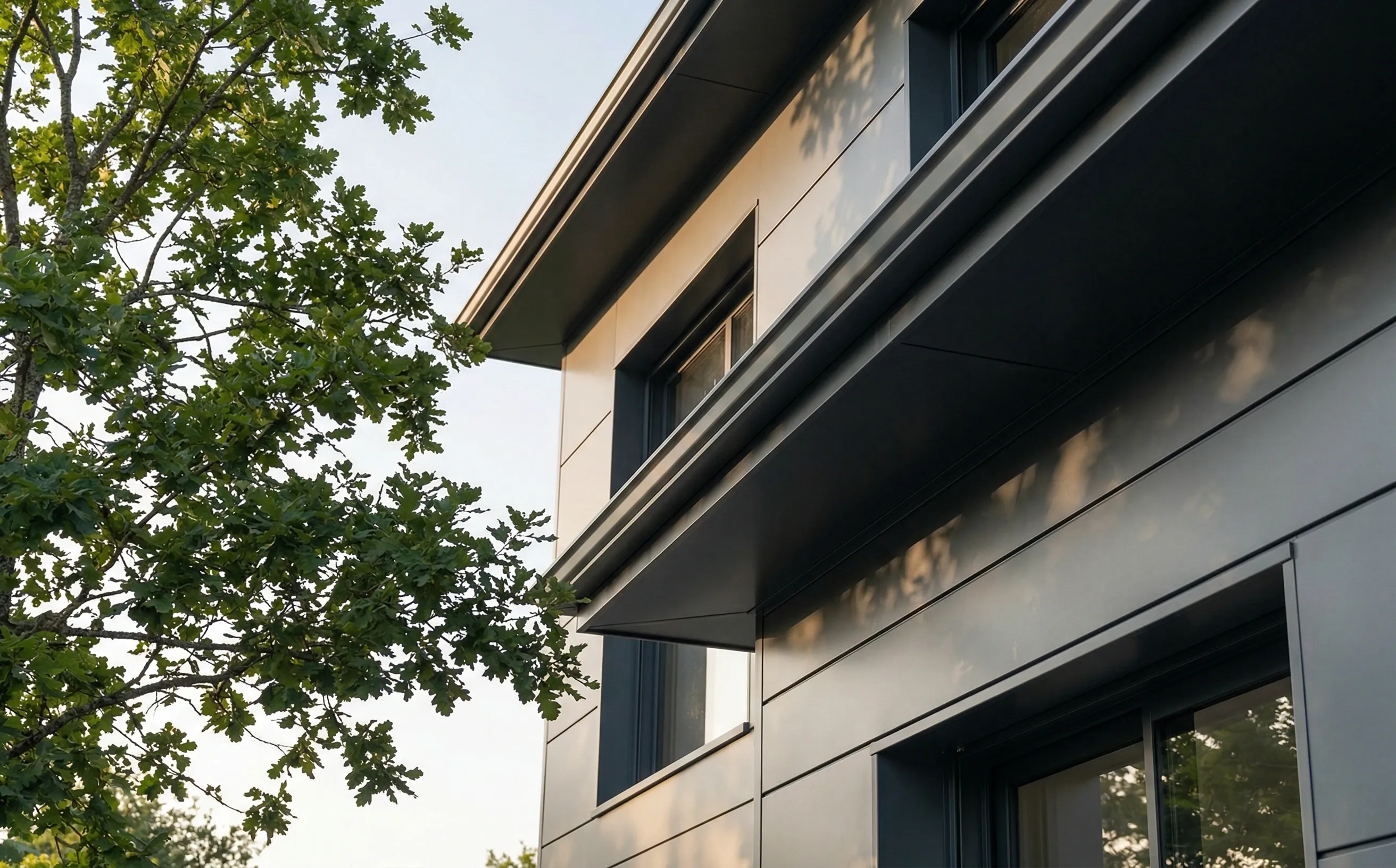 Sous-face en aluminium laqué gris anthracite sous le débord d'une maison moderne avec gouttière assortie, menuiseries foncées et chêne dans le jardin